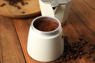 Moka pot with ground coffee and beans on wooden table, closeup