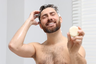 Photo of Happy man showing solid shampoo bar in bathroom
