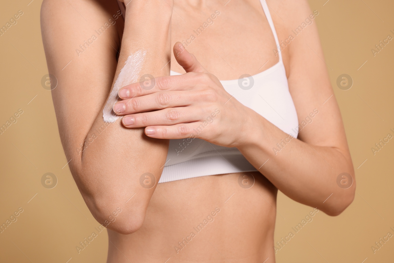 Photo of Woman applying body cream onto her arm against beige background, closeup