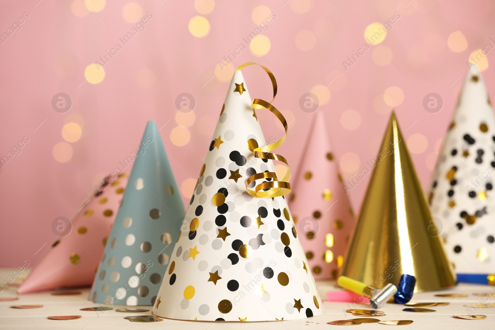 Photo of Party hats and festive items on white table against pink background with blurred lights