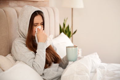 Photo of Sick young woman with cup of hot drink in bed at home. Influenza virus