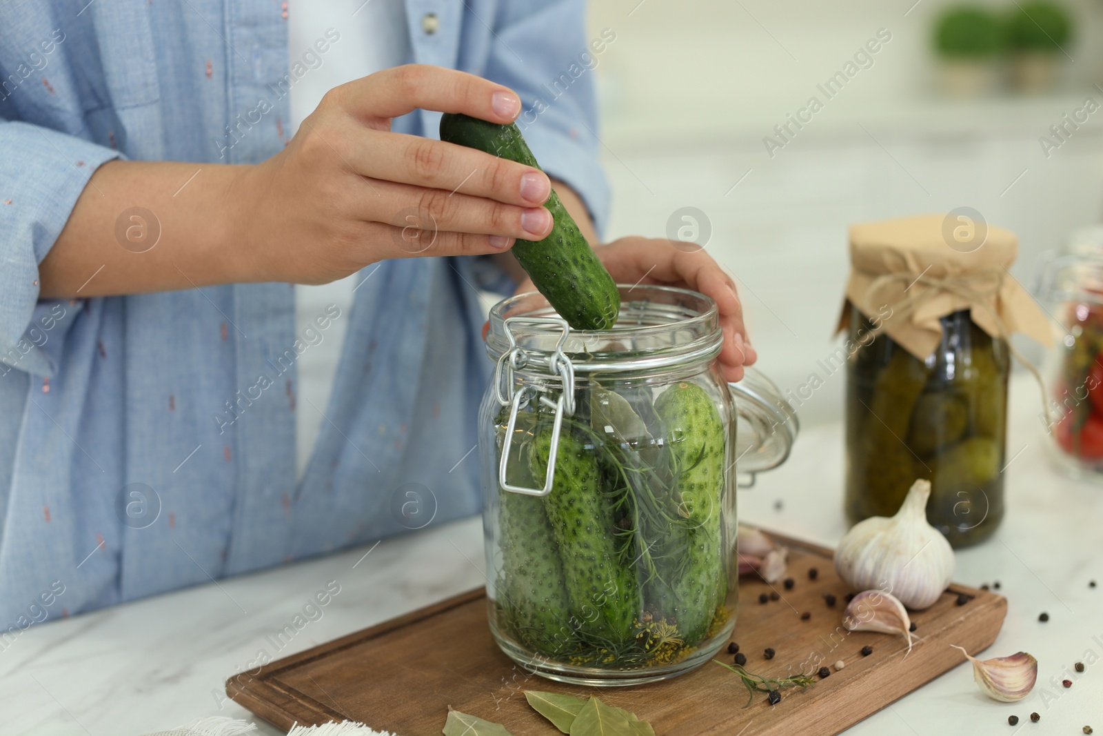 Photo of Woman putting cucumber into pickling jar at table in kitchen, closeup