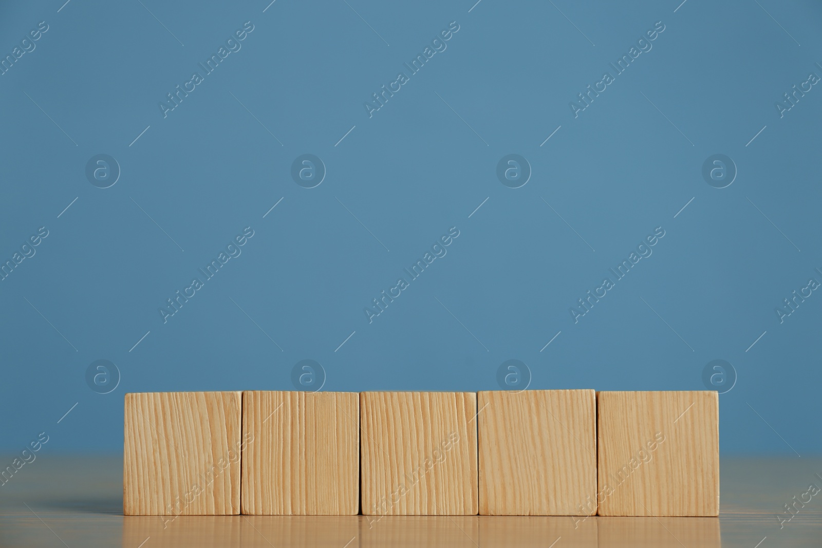 Photo of Row of blank cubes on wooden table against light blue background. Space for text