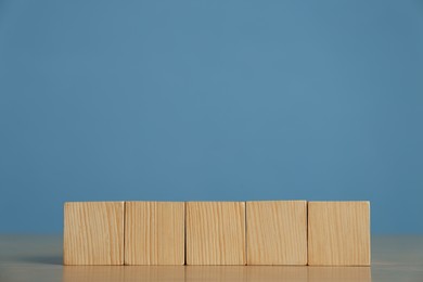 Photo of Row of blank cubes on wooden table against light blue background. Space for text