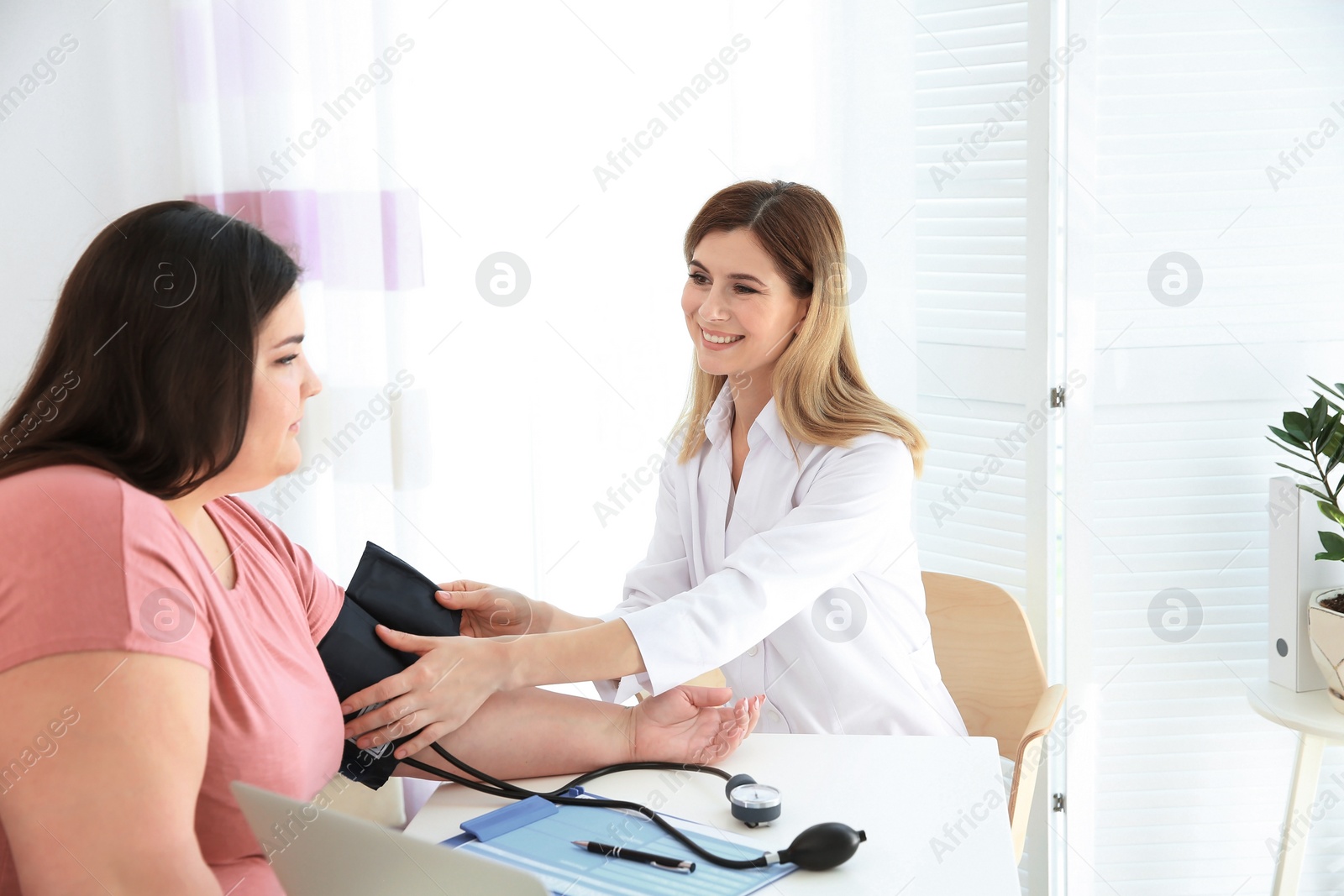 Photo of Female doctor measuring blood pressure of overweight woman in clinic