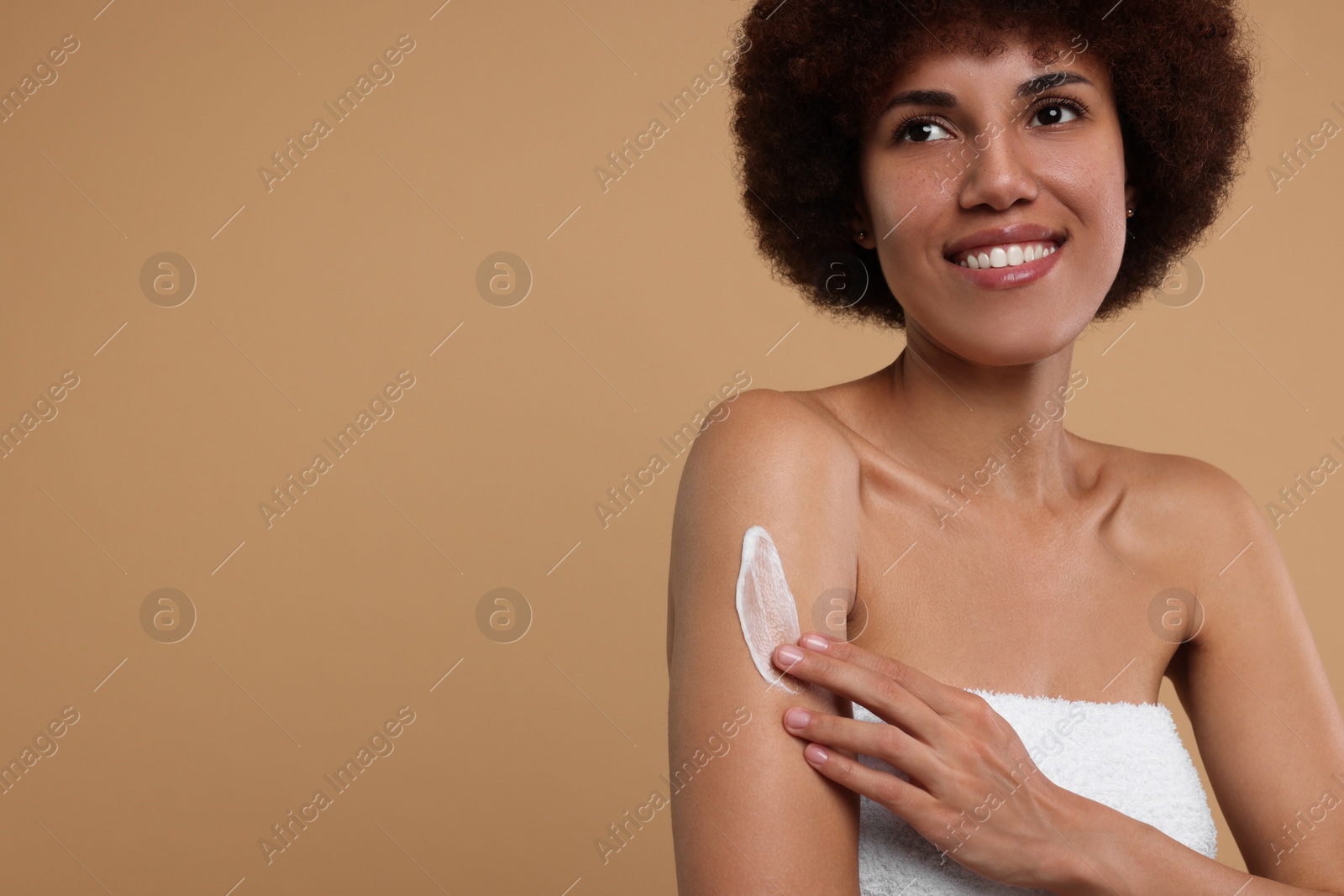 Photo of Beautiful young woman applying body cream onto arm on beige background, space for text