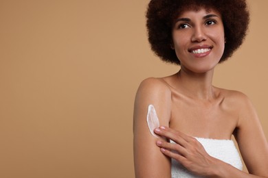 Beautiful young woman applying body cream onto arm on beige background, space for text