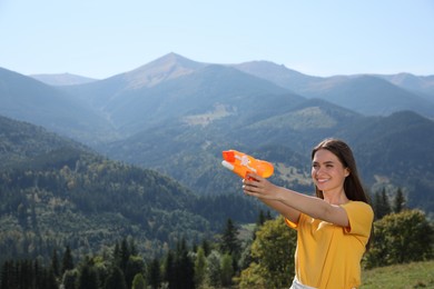 Happy woman with water gun having fun in mountains on sunny day