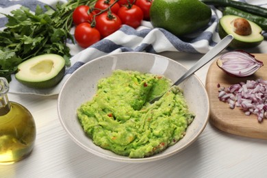 Delicious guacamole in bowl and ingredients on white wooden table, closeup