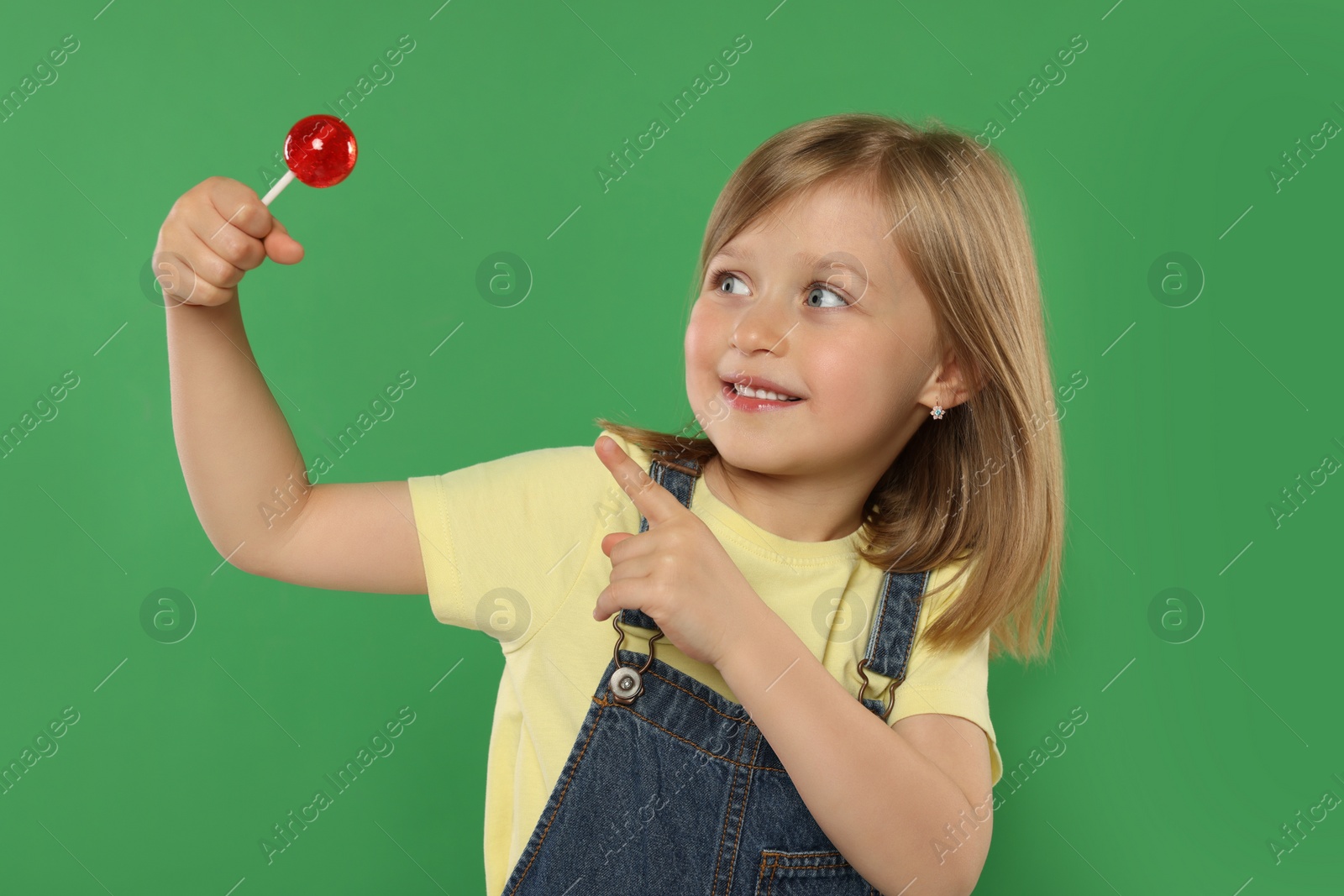 Photo of Portrait of cute girl pointing at lollipop on green background