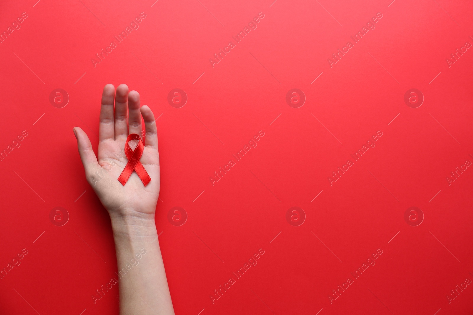 Photo of Woman holding red awareness ribbon on color background, top view with space for text. World AIDS disease day