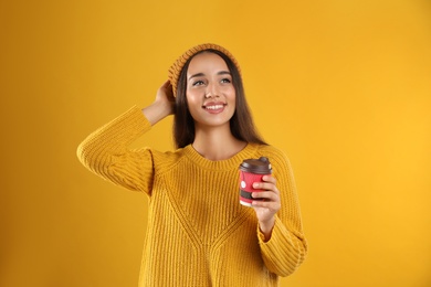 Happy beautiful woman with paper cup of mulled wine on yellow background