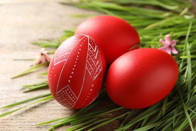 Photo of Red painted Easter eggs and green grass on wooden table, closeup