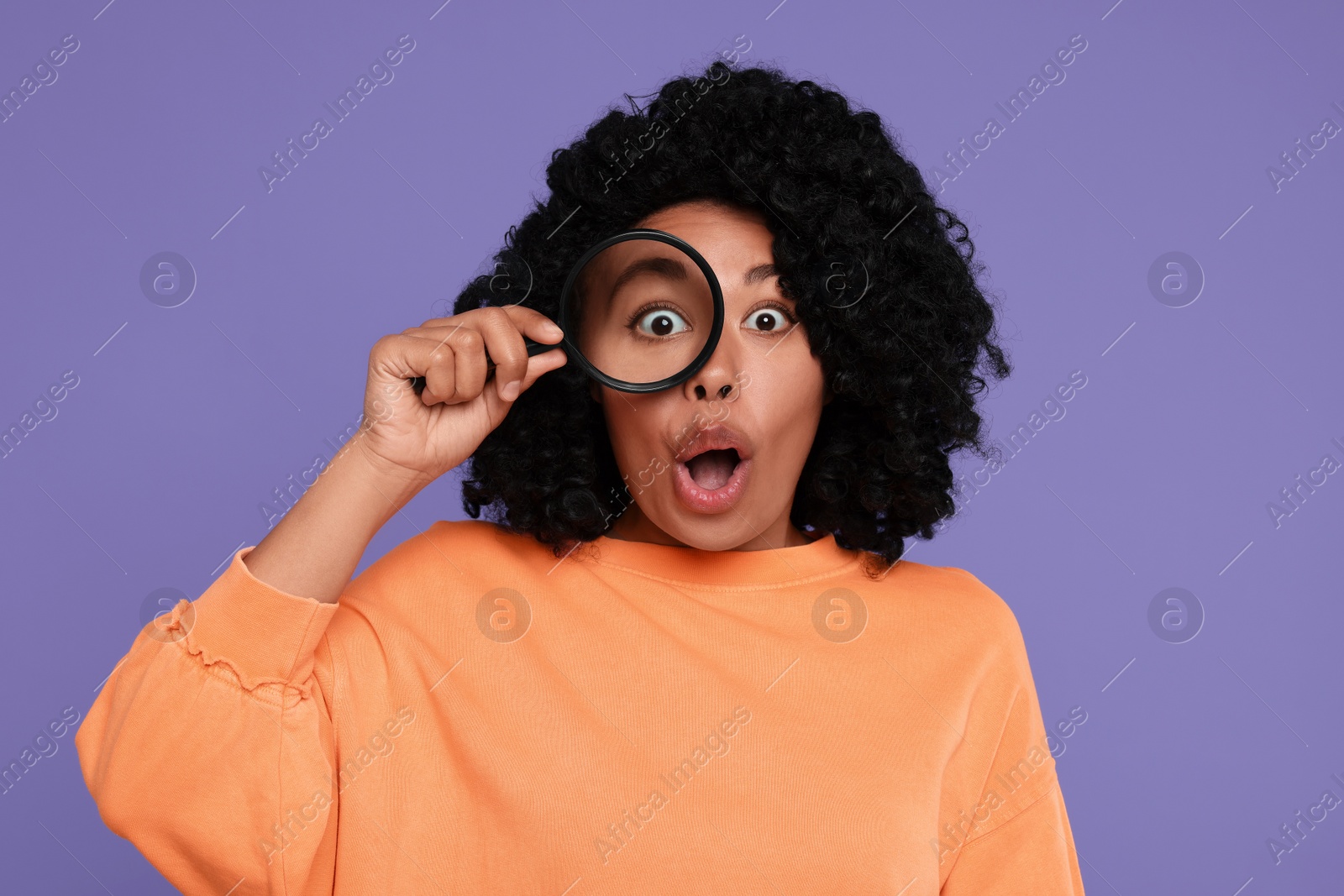Photo of Emotional woman looking through magnifier glass on purple background