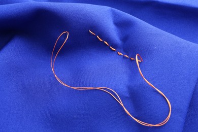 Photo of Sewing needle with thread and stitches on blue cloth, closeup