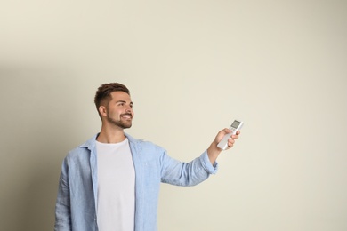 Photo of Happy young man operating air conditioner with remote control on beige background. Space for text