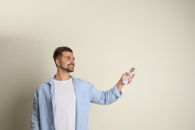 Happy young man operating air conditioner with remote control on beige background. Space for text