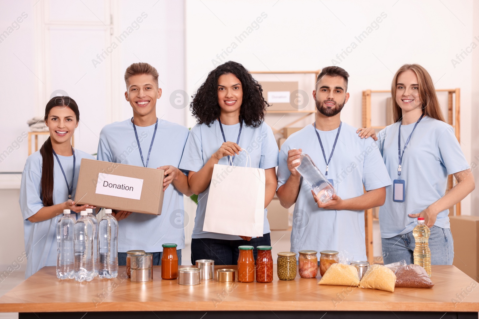 Photo of Portrait of volunteers with donation box, paper bag and food products at table in warehouse