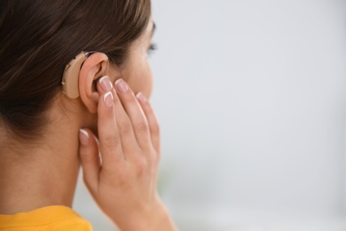 Young woman with hearing aid indoors, closeup. Space for text