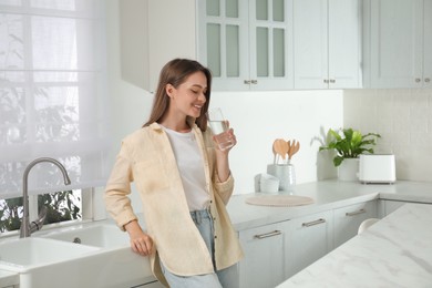 Photo of Woman drinking tap water from glass in kitchen