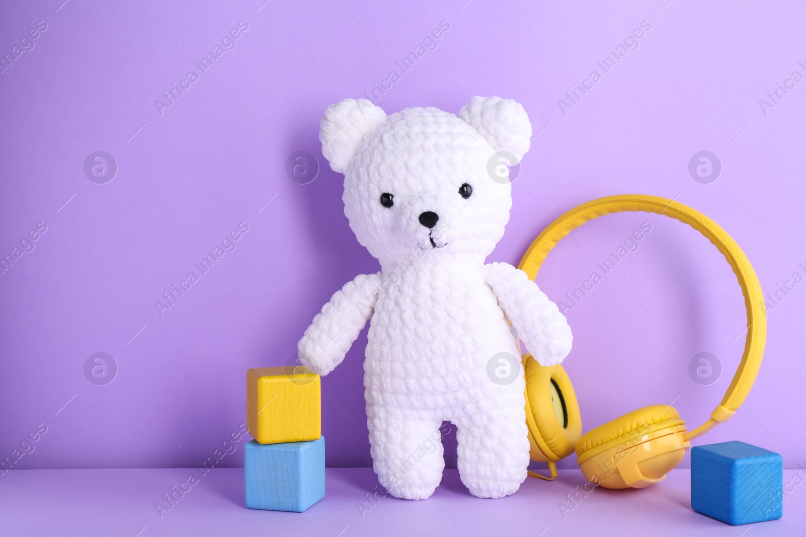 Photo of Baby songs. Toy bear, headphones and cubes on violet background