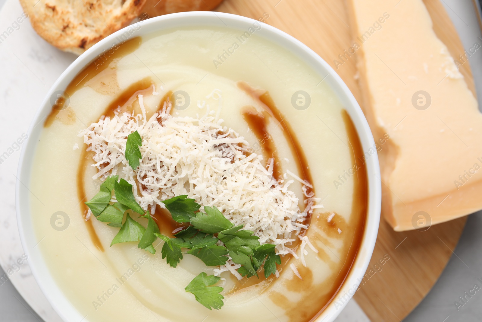 Photo of Delicious cream soup with parmesan cheese, soy sauce and parsley in bowl on light grey table, flat lay