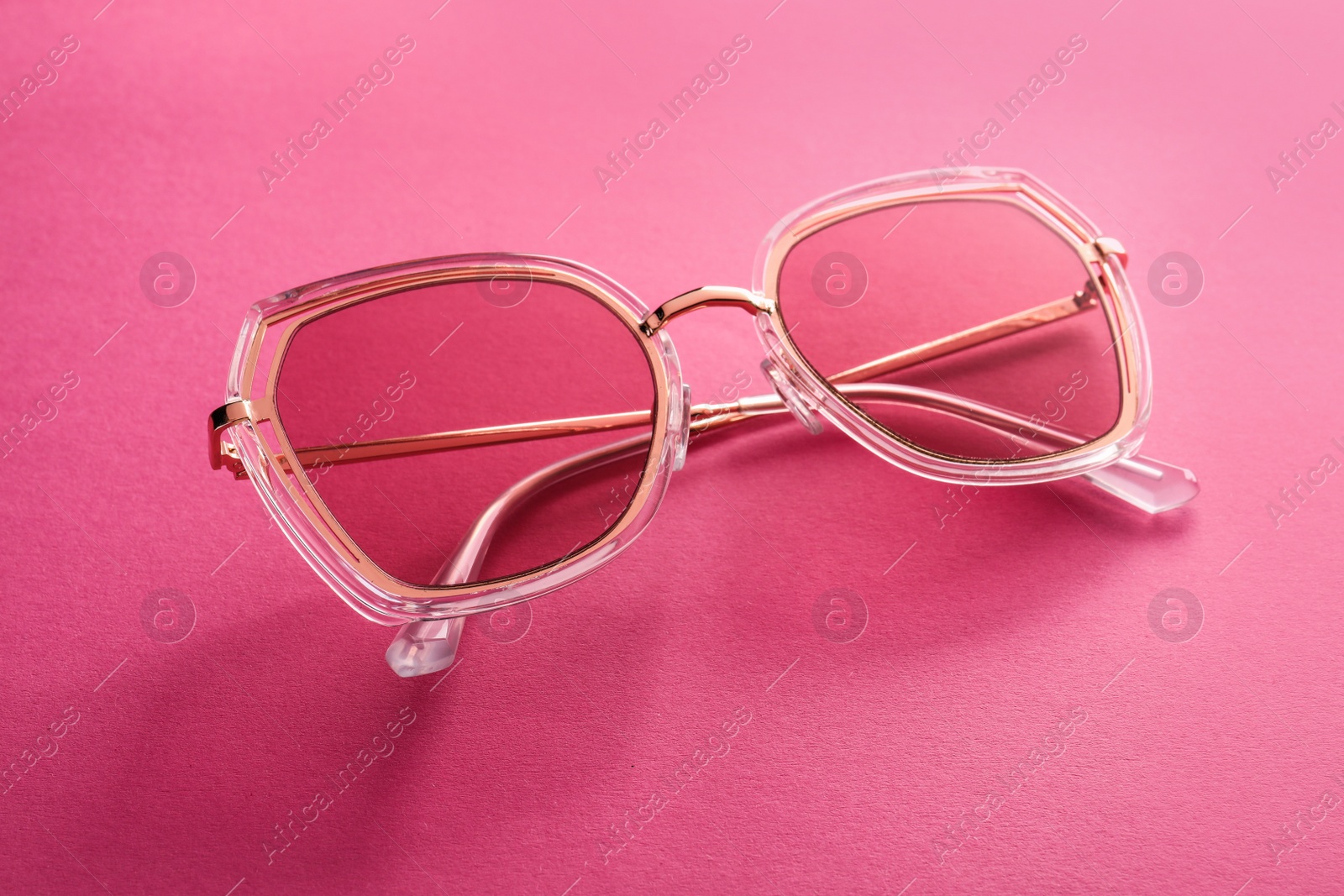 Photo of New stylish sunglasses on pink background, closeup. Fashionable accessory