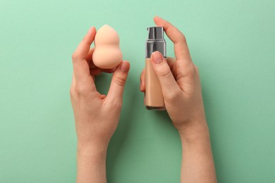 Photo of Woman with makeup sponge and skin foundation on mint color background, top view
