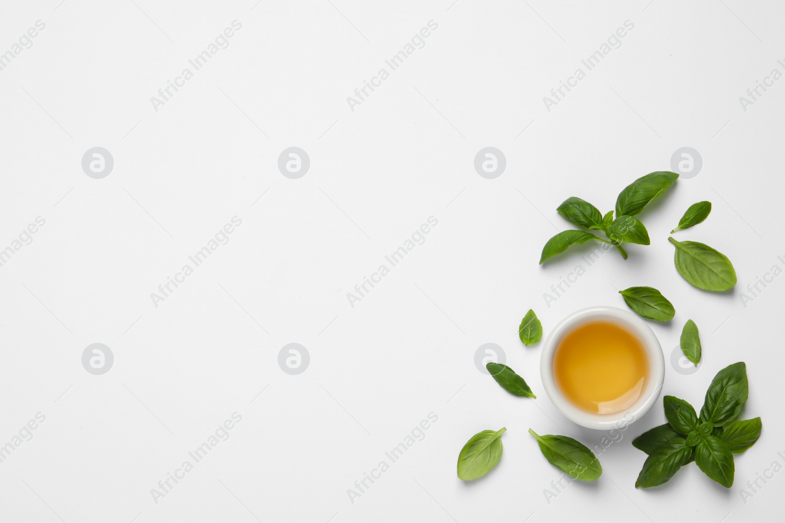 Photo of Essential basil oil and fresh leaves on white background, flat lay. Space for text