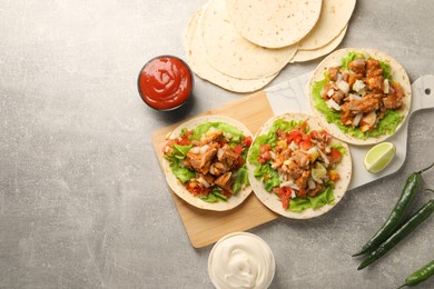 Delicious tacos with vegetables, meat and sauce on grey textured table, flat lay. Space for text