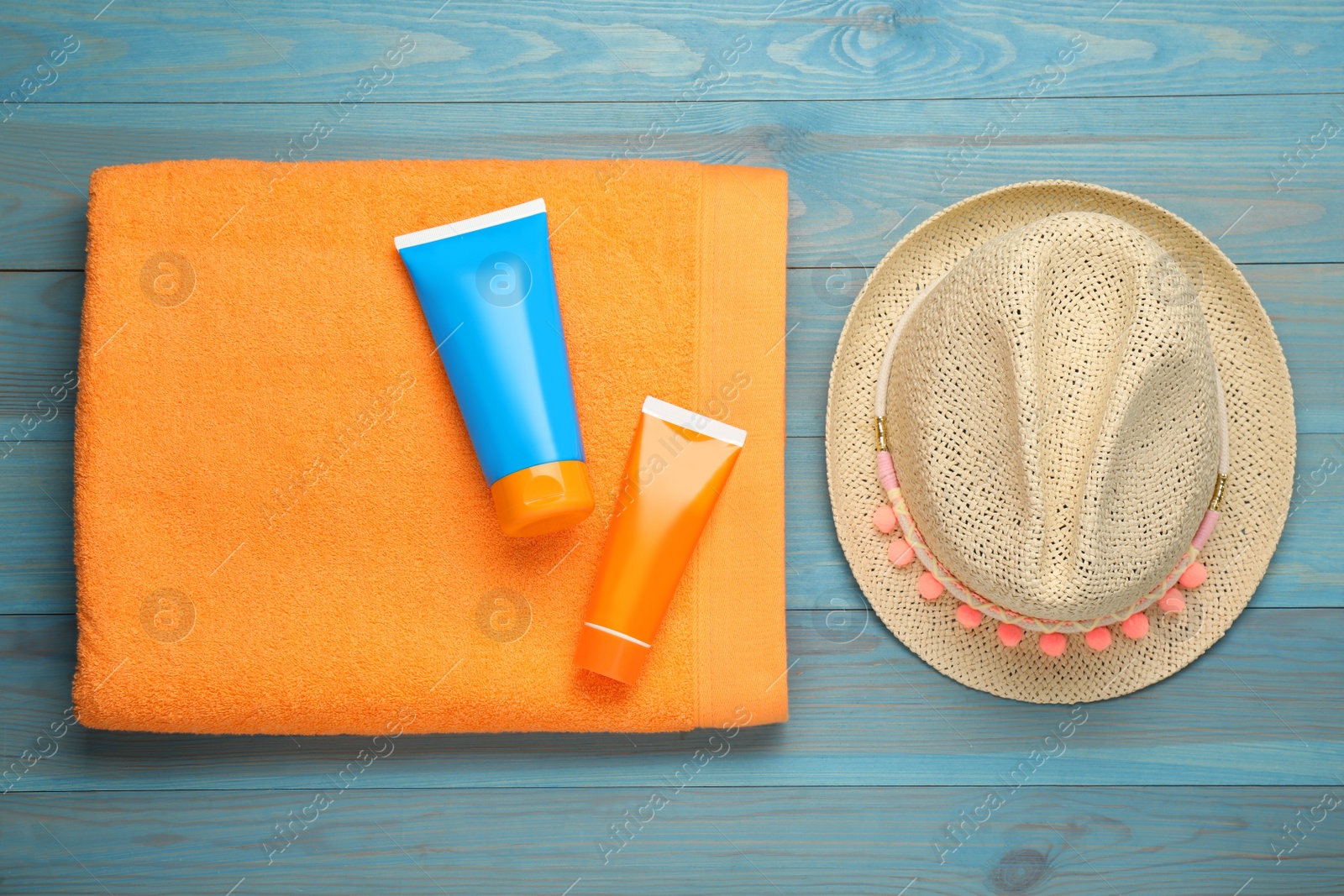 Photo of Beach towel, straw hat and sun protection products on light blue wooden background, flat lay