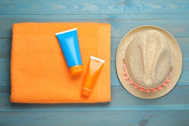 Beach towel, straw hat and sun protection products on light blue wooden background, flat lay