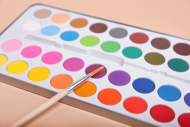 Photo of Watercolor palette with brush on beige background, closeup