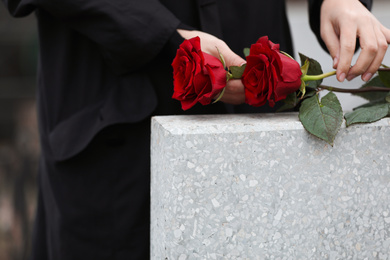 Photo of Woman with red roses near light grey tombstone outdoors, closeup. Funeral ceremony