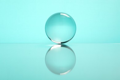 Photo of Transparent glass ball on mirror surface against turquoise background