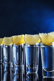 Shot glasses of vodka with lemon slices on dark blue background