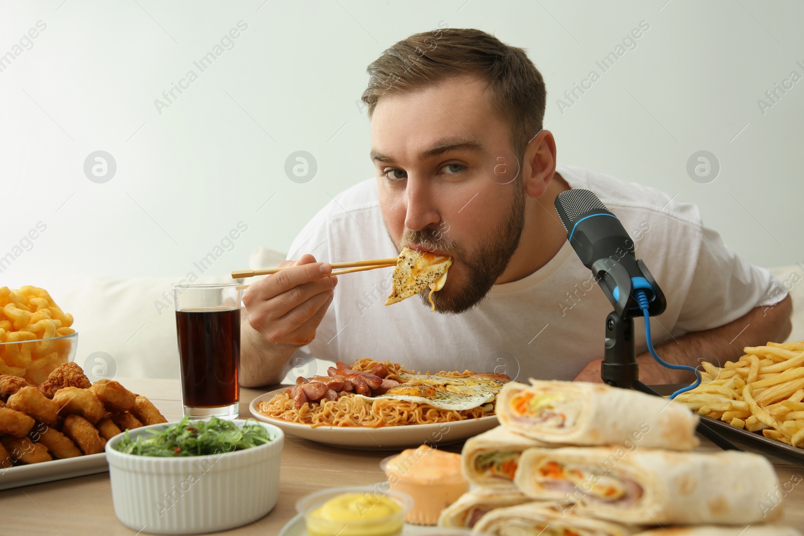 Photo of Food blogger eating in front of microphone at table against light background. Mukbang vlog