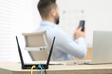 Photo of Man with smartphone working at wooden table indoors, focus on Wi-Fi router