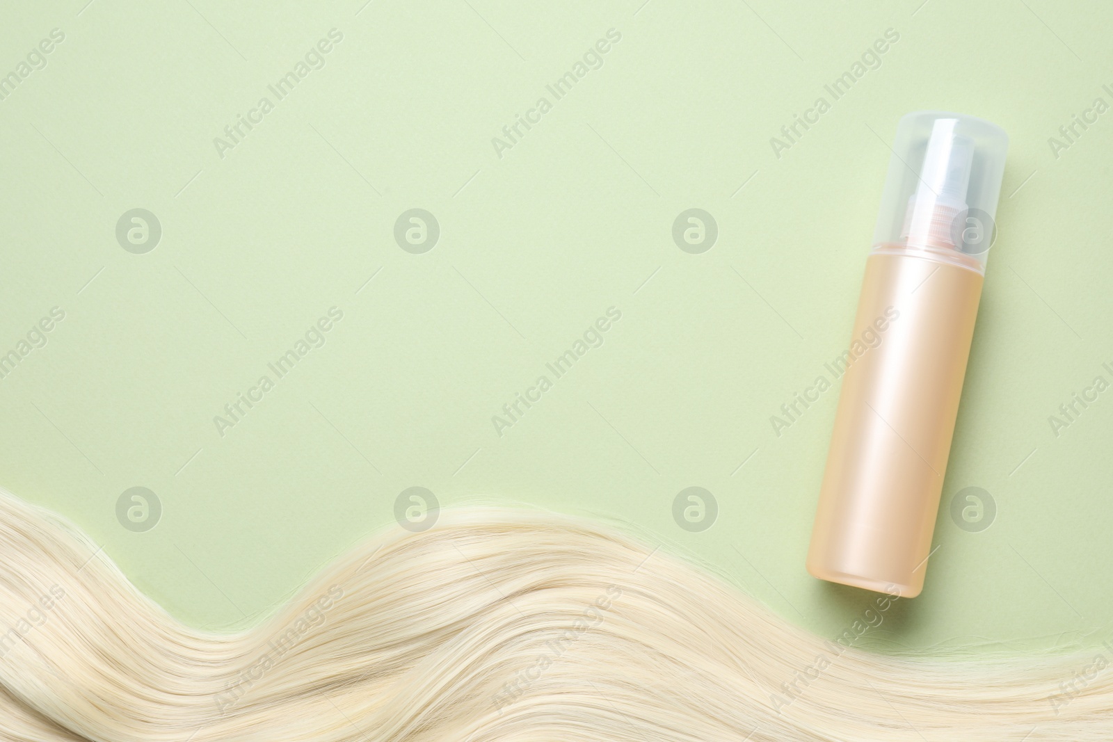 Photo of Spray bottle with thermal protection and lock of blonde hair on pale green background, flat lay. Space for text
