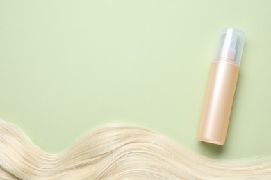Spray bottle with thermal protection and lock of blonde hair on pale green background, flat lay. Space for text