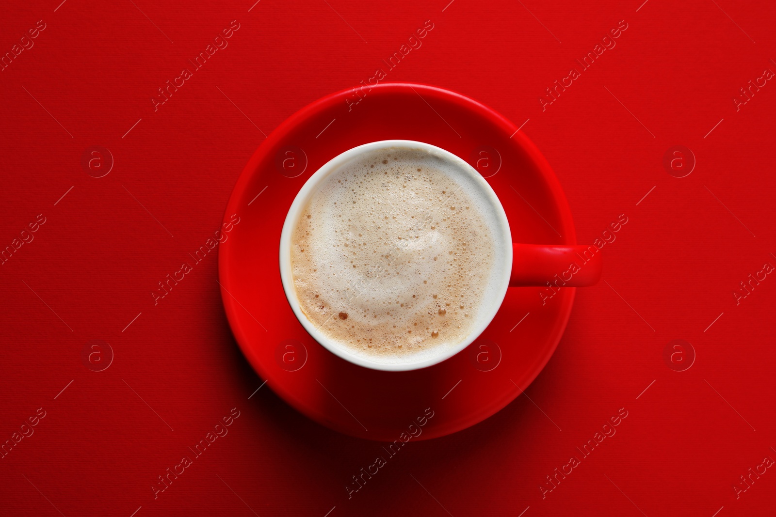 Photo of Cup with aromatic cappuccino on red background, top view