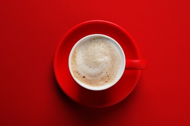Photo of Cup with aromatic cappuccino on red background, top view