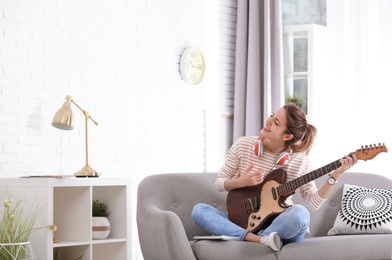Photo of Young woman with headphones playing electric guitar in living room. Space for text