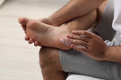 Photo of Man with dry skin applying cream onto his foot on bed, closeup