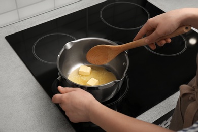 Photo of Woman stirring butter in saucepan on electric stove, closeup