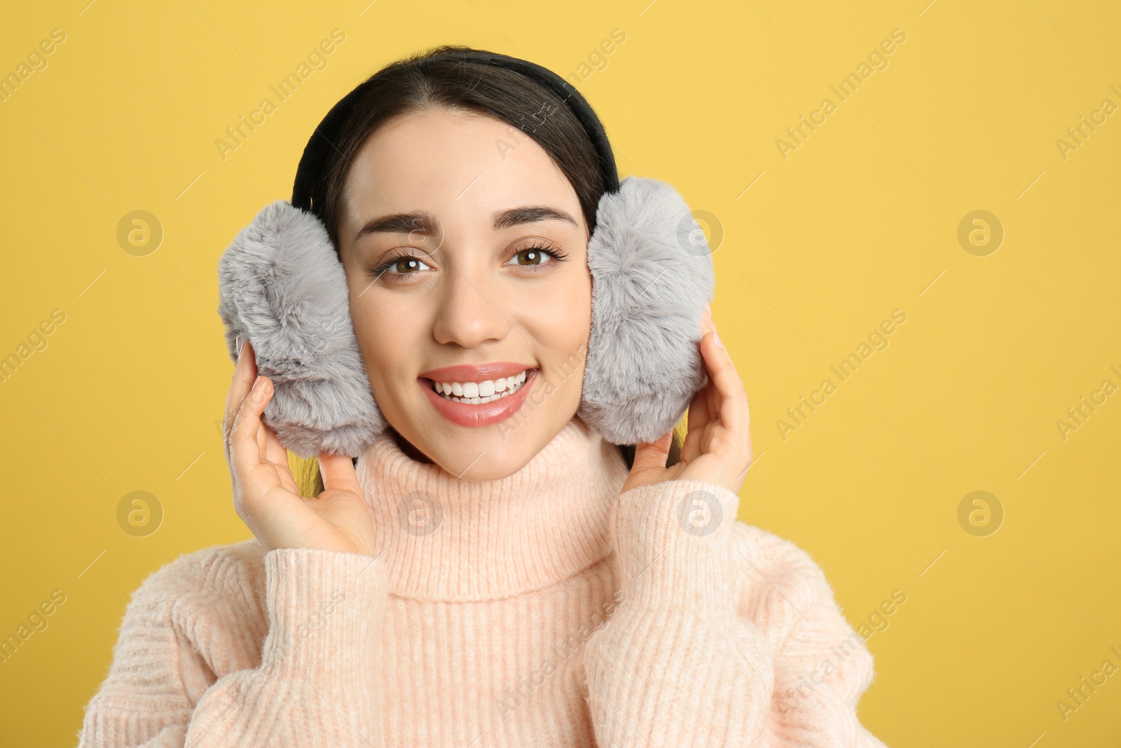 Photo of Beautiful young woman wearing earmuffs on yellow background