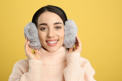 Beautiful young woman wearing earmuffs on yellow background