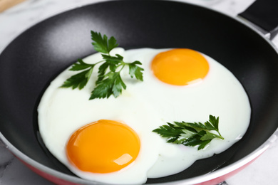 Photo of Tasty cooked chicken eggs with parsley in frying pan, closeup