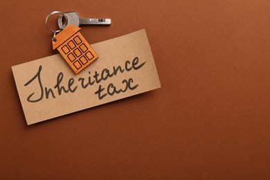 Photo of Card with phrase Inheritance Tax and key with house shaped key chain on brown background, top view. Space for text