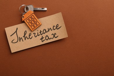 Card with phrase Inheritance Tax and key with house shaped key chain on brown background, top view. Space for text